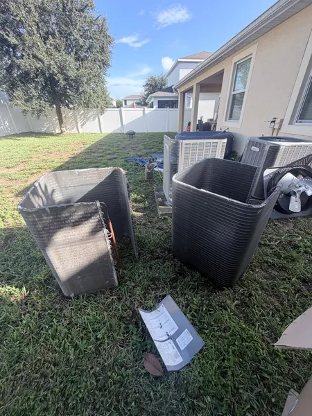 Two old, weathered condenser coil sections and cabinet panels lying on a backyard lawn after being removed during an AC system changeout