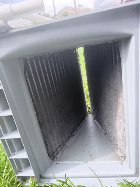 Inside of an outdoor condenser cabinet with a dirty, dust-covered condenser coil before cleaning