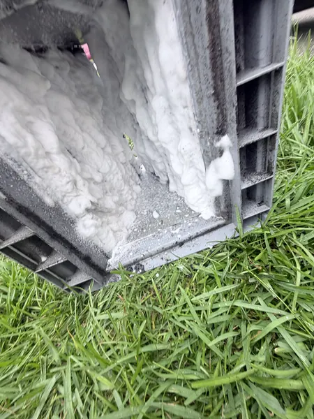 Condenser coil covered in white foaming coil cleaner during cleaning